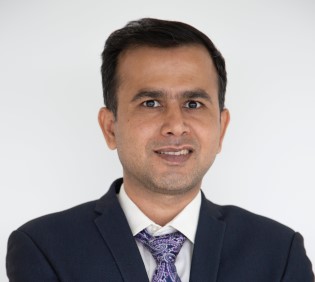 Person in a suit with a patterned tie, smiling against a plain background.
