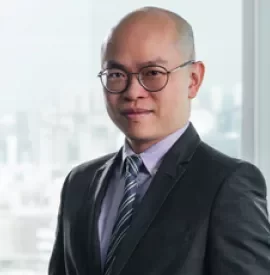 Person in a suit and tie standing in front of a window with city view.