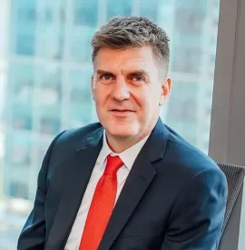 Smiling person in a suit and red tie by a window.