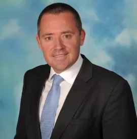 Professional headshot of a person in a suit and tie with a blue background.