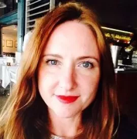 Person with long hair and red lipstick smiling in a restaurant.