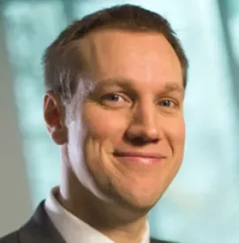 Person in a suit smiling with a blurred background.