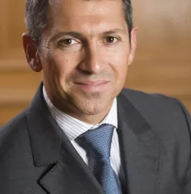 Person in a suit with a striped shirt and tie, smiling at the camera.