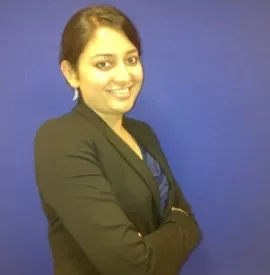 Smiling person in a black blazer against a blue background.