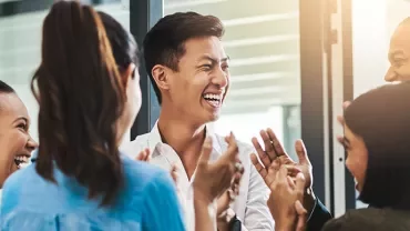 Group of people laughing and clapping in a bright office.