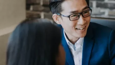 Person in a blue suit smiling during a conversation indoors.