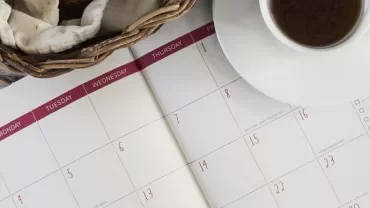 Open calendar with coffee cup and bread basket.