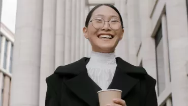 Person smiling with a coffee cup, standing in front of tall columns.