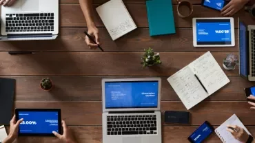 Top view of people working with laptops and tablets on a wooden table.