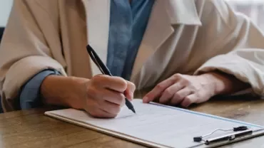Person signing a document at a wooden desk with a pen.