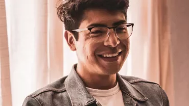 Person smiling while wearing glasses and a denim jacket.