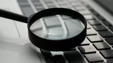 Magnifying glass hovering over a laptop keyboard.