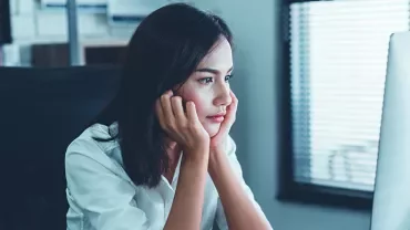Person seated at a desk, looking intently at a computer screen in a modern office.