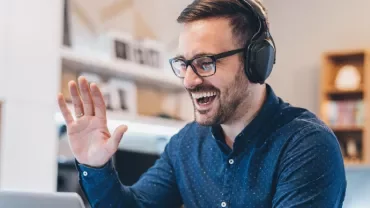 Person wearing headphones and glasses, smiling at a laptop.
