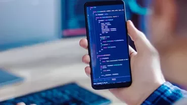 Person holding a smartphone displaying lines of code on the screen.