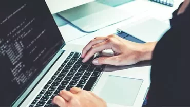Person typing on a laptop with code on screen.