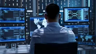 Person working with multiple digital screens in a control room.