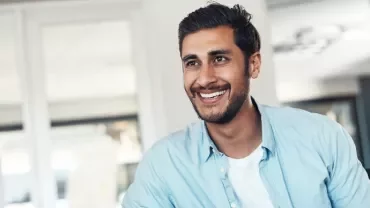 Person smiling in an office setting with glass walls in the background.
