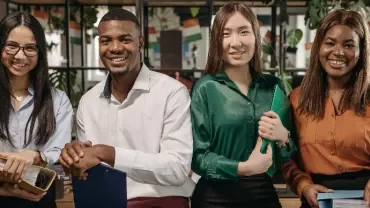 Four people smiling in an office setting, holding folders.