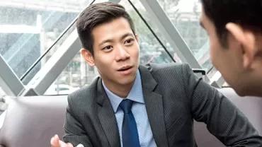 Two people in suits having a discussion in a modern office setting.