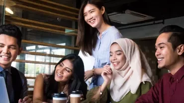 Group of people smiling and looking at a laptop in an office.