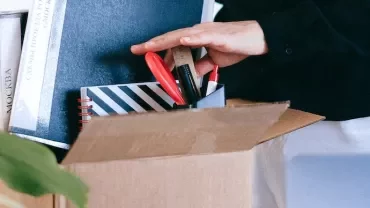 Person packing files and office supplies into a cardboard box.