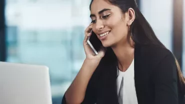 Person smiling while talking on a phone and using a laptop.