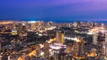 Aerial view of a city skyline at dusk with skyscrapers and illuminated streets.