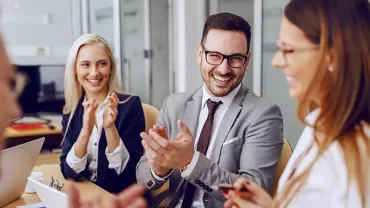 Group of professionals smiling and clapping in a meeting room.
