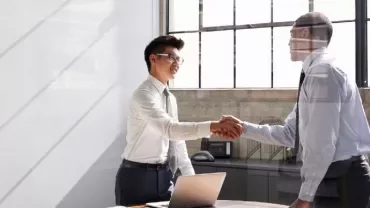 Two people shaking hands in a bright office setting.