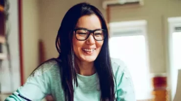 Person smiling while looking at a computer in a cozy room.
