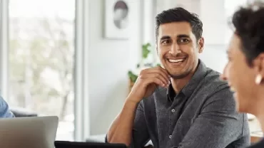 People sitting at a table with laptops, engaged in a discussion.
