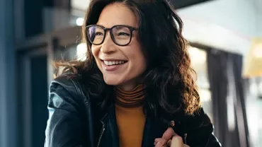 Person smiling in a well-lit room with glasses and a leather jacket.