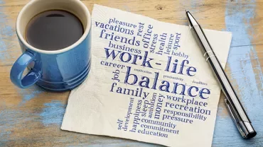 Coffee cup and pen next to napkin with words about work-life balance.