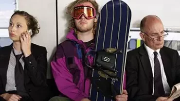 Three people sit on public transport, one holding a snowboard.