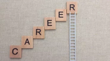 Scrabble tiles spell 'career' on a step pattern with a ladder symbolizing growth.