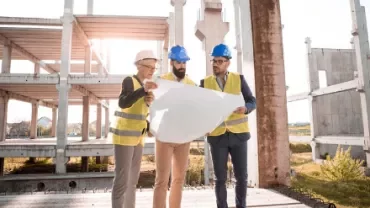 Three construction workers examining blueprints at a building site.