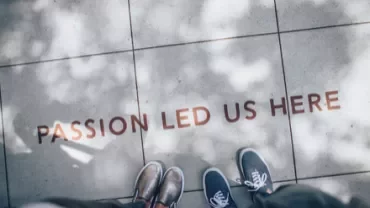 Two people standing on a tiled path with 'Passion Led Us Here' written on the ground.