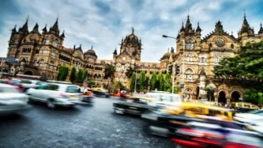 Blurry traffic in front of a large historical building with cloudy sky.