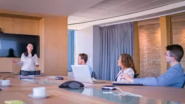 Person presenting in a modern conference room with colleagues listening attentively.