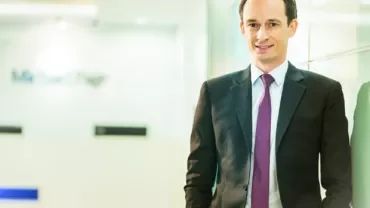 Person in a suit with a purple tie standing in a bright office space.