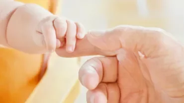 Adult hand gently holding a small child's hand.