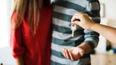 Person handing over house keys to another individual.