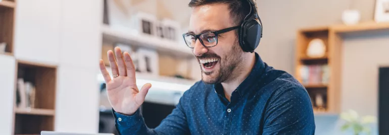 image of male white collar employee sitting in front of a laptop smiling waving