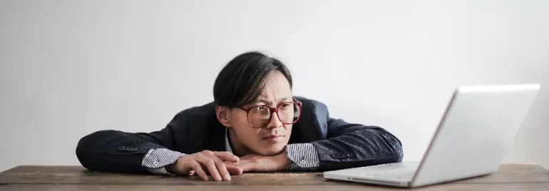 Person with glasses looking intently at a laptop on a wooden table.