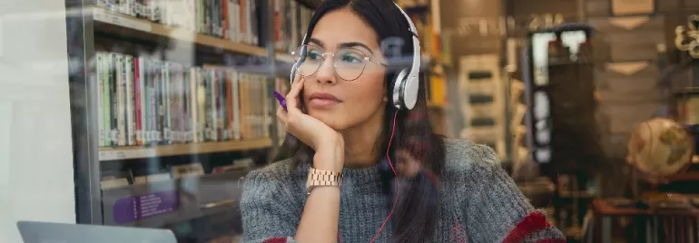 an East Asian woman in glasses looking out of a cafe, with headphones on