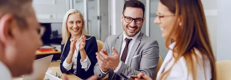 Group of professionals smiling and clapping in a meeting room.