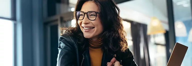 Person smiling in a well-lit room with glasses and a leather jacket.