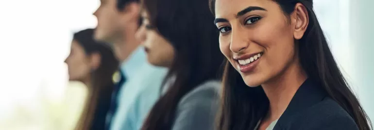 A woman in business attire smiles at the camera, sitting in a row with three other people, all facing forward in a professional setting.
