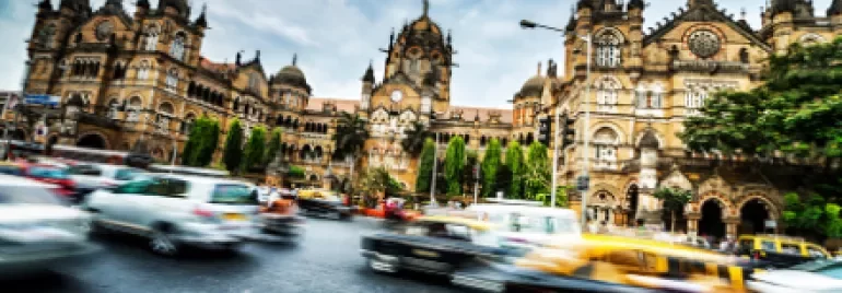 Blurry traffic in front of a large historical building with cloudy sky.
